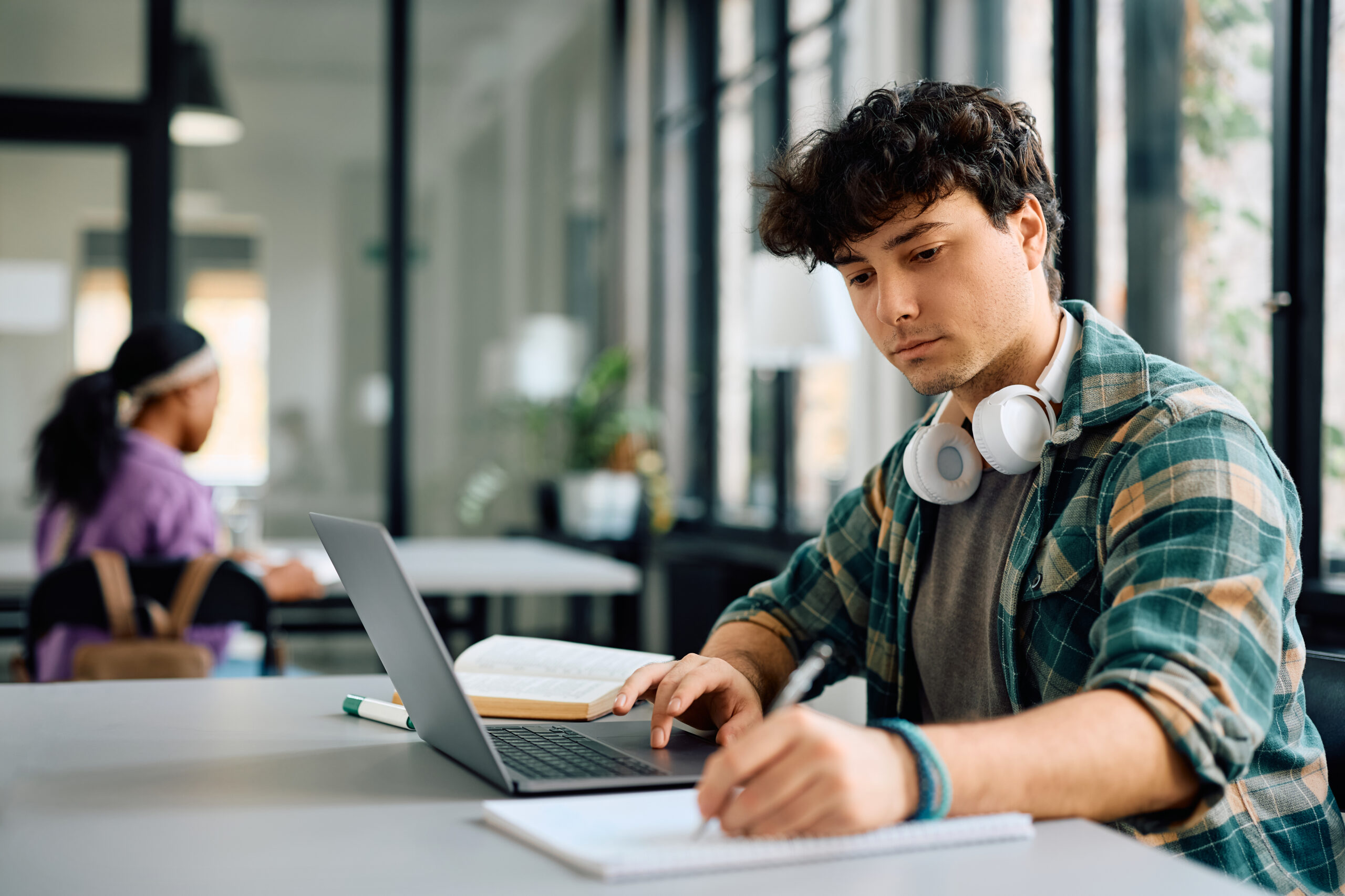 University student writing while using laptop and studying in the classroom. Copy space.