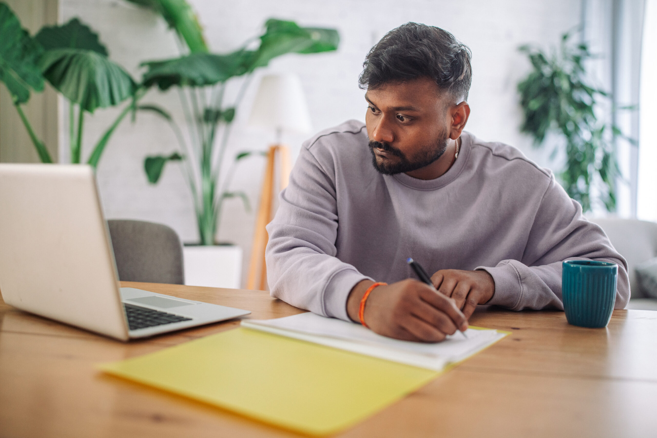 Young indian man focused on work with laptop and notepad in a cozy home setting