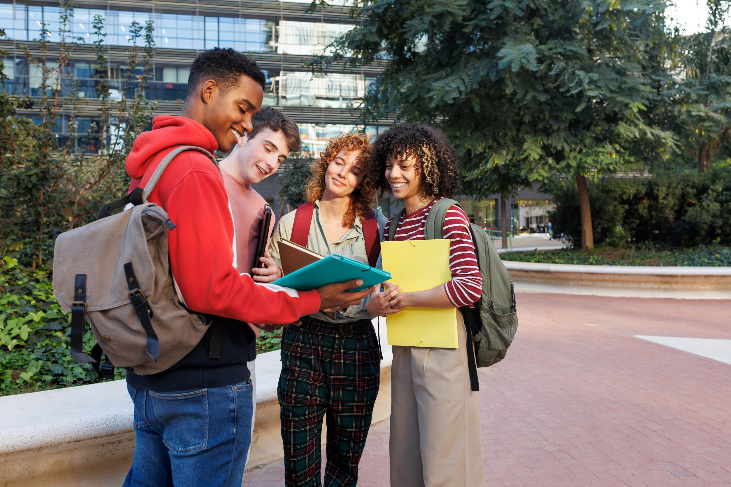 Four cheerful diverse university students collaborating on a project, sharing ideas and information outdoors on campus