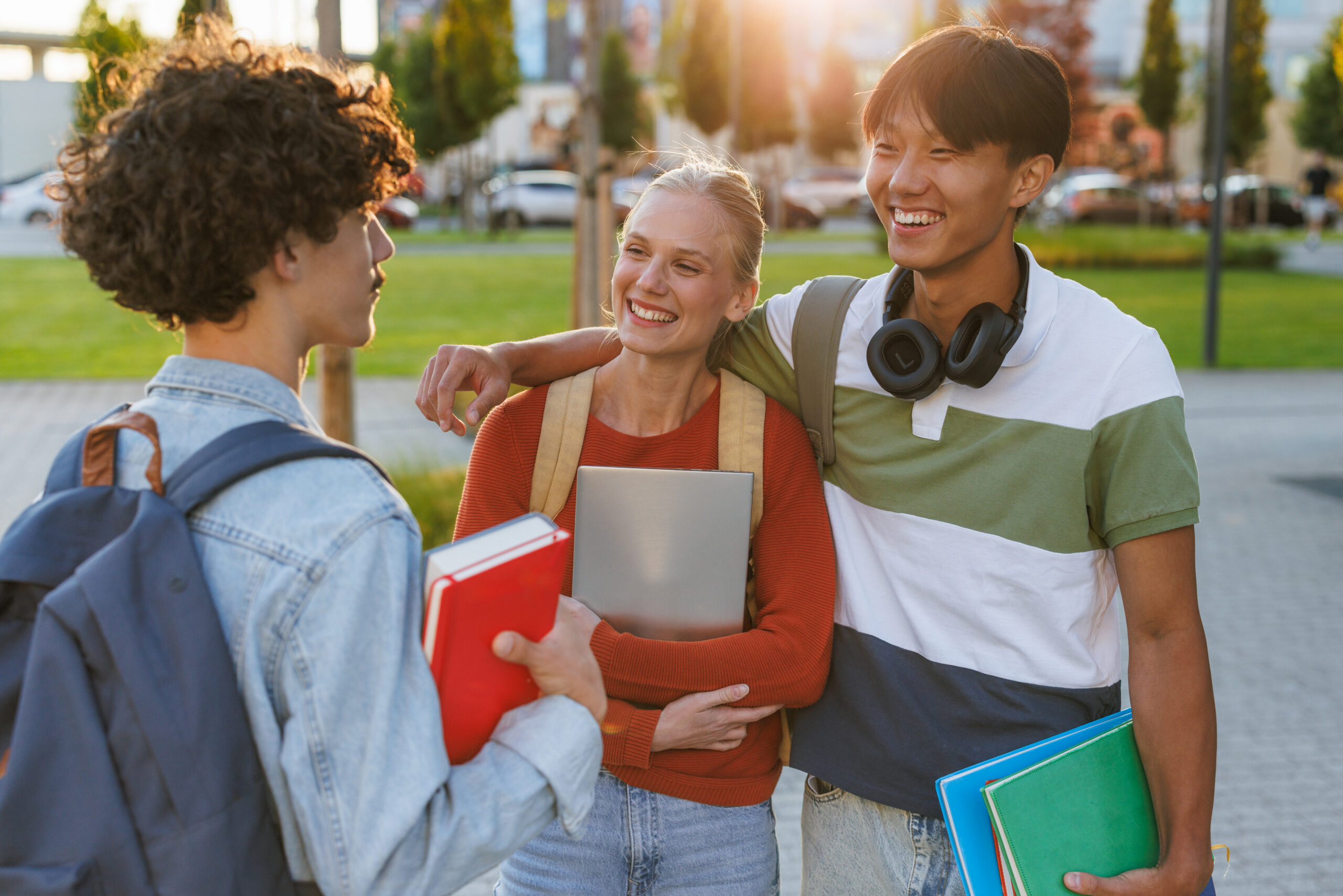 A cheerful group of young students gathered outdoors at a university campus, enjoying conversation. They are holding books and look engaged, depicting a moment of friendship and academic connection.